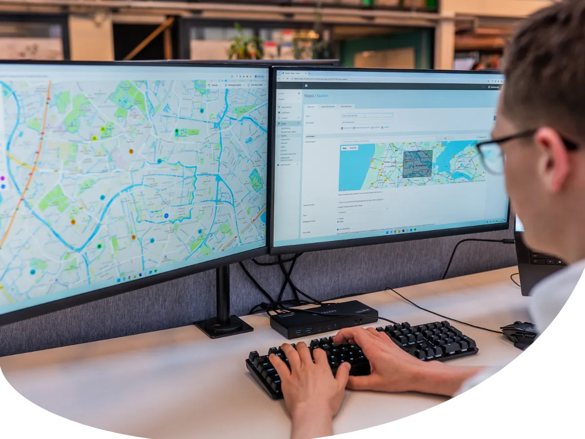 Foto van developer achter 2 computer schermen met kaarten op het scherm